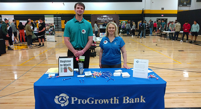 Two members of the ProGrowth team standing behind a table in a high school gym