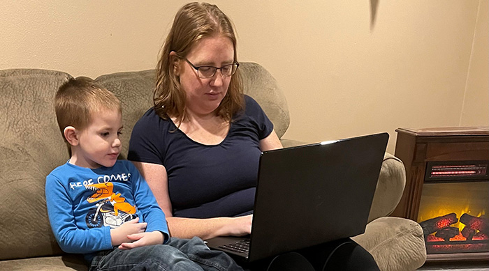 Woman and her son sitting on a couch. The woman is working on her laptop